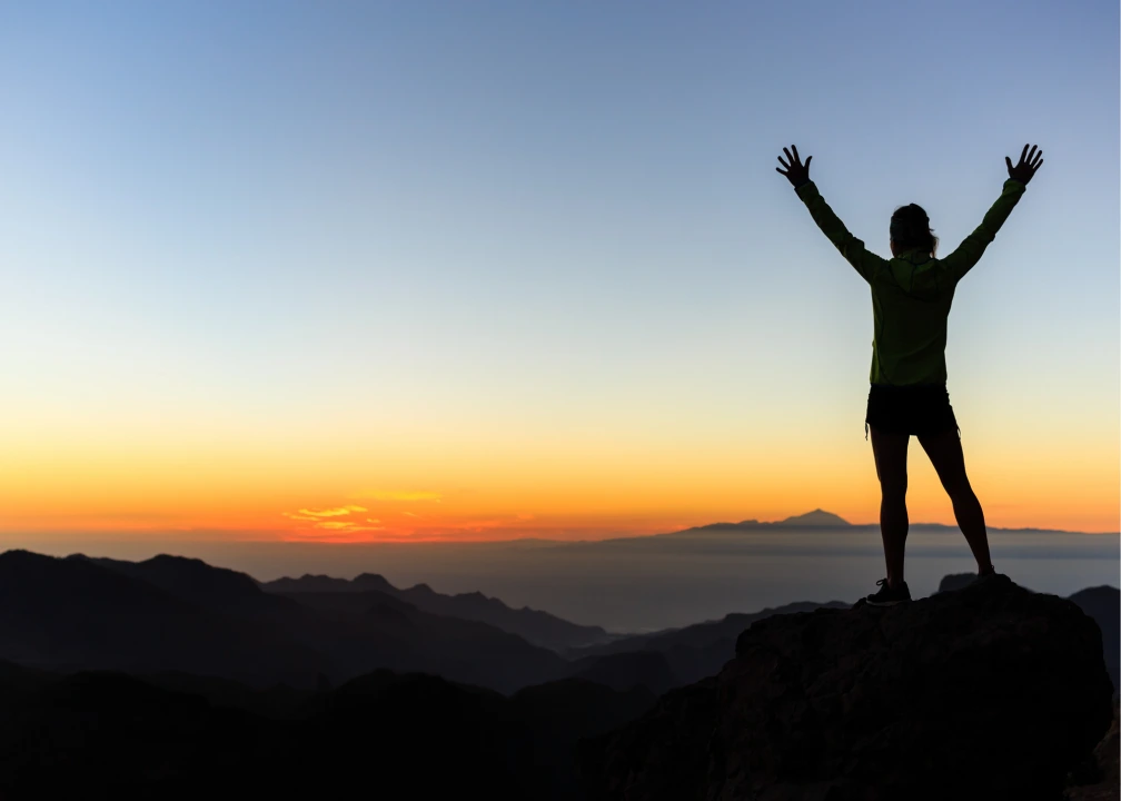 Una persona in cima ad una rupe allarga le braccia in segno di vittoria, è contento del suo peso forma